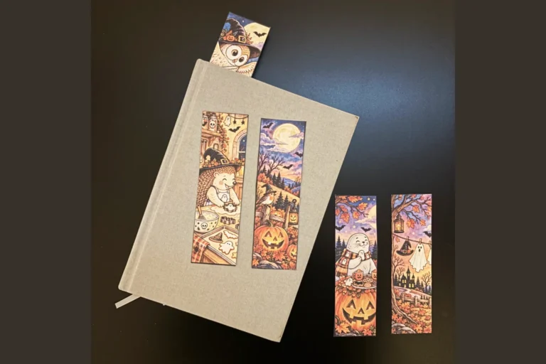 Utskrivna Halloweenbokmärken från Nordisk Lagom med uggla, igelkott, säl, pumpor och höstmotiv, placerade på och bredvid en bok.